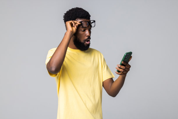 惊喜。震惊的年轻非洲人使用智能手机，而站在孤立的灰色背景图片下载
