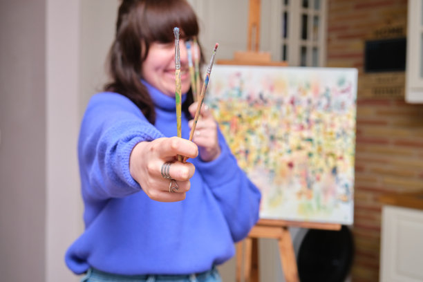 年轻快乐的女人拿着画笔挡在面前，选择性地聚焦。图片下载