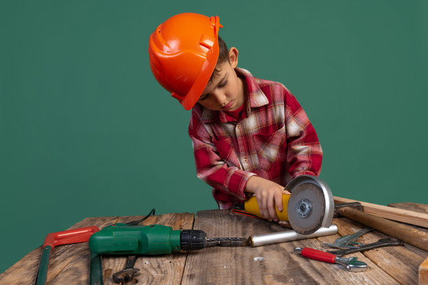 可爱的小男孩肖像，建筑工人的孩子形象，设计师在橙色的防护头盔使用工作工具孤立在绿色的背景图片下载