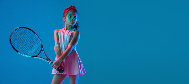 工作室拍摄的小女孩，初学者网球运动员训练孤立在蓝色工作室背景下霓虹灯。运动、学习、童年观念图片下载