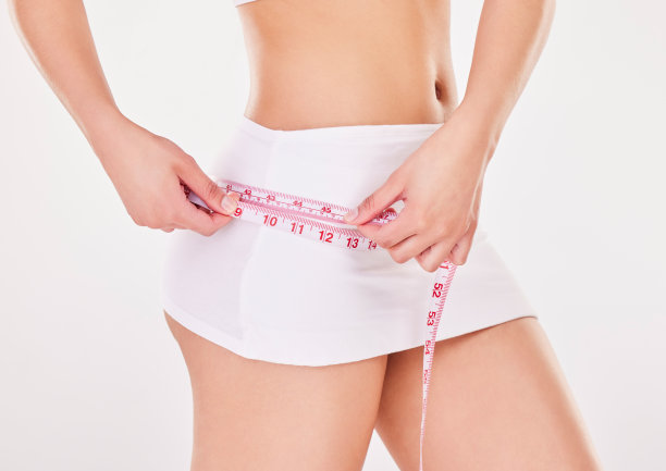 工作室拍摄的一个不认识的年轻女子使用测量卷尺对灰色的背景图片下载