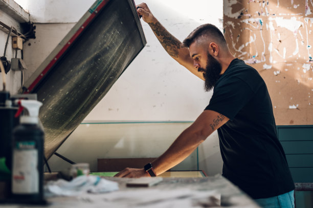 在印刷车间工作时使用屏幕曝光设备的男性工人图片下载