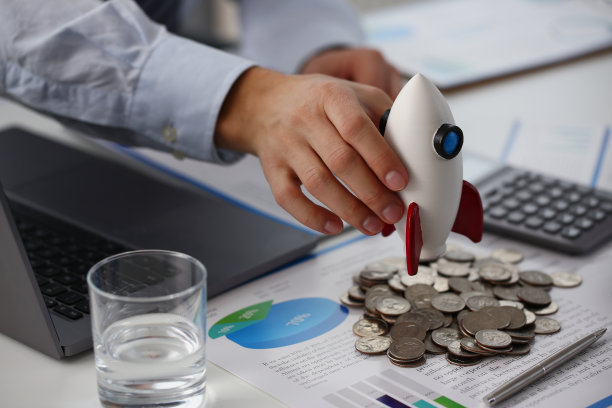 人们把火箭模型放在桌上的一堆硬币和商业文件上图片下载