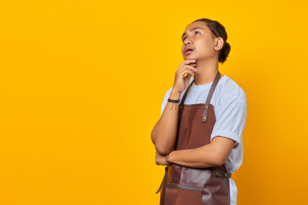 有吸引力的英俊年轻的咖啡师托下巴与举起的手和仰望孤立的黄色背景图片下载