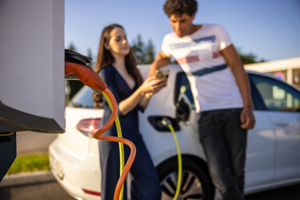 一对夫妇一边用手机一边给电动车充电图片下载