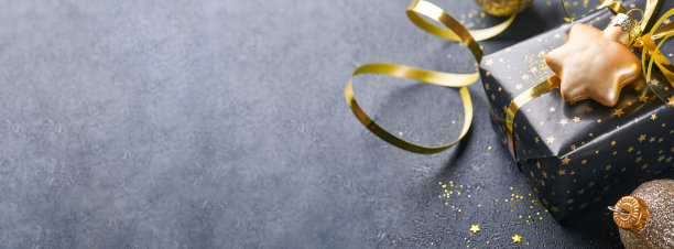 假日礼品盒或礼品带，金色的纸屑和金色的小玩意在黑色的背景上。神奇的圣诞贺卡。圣诞装饰。边界设计。模拟。横幅。图片下载