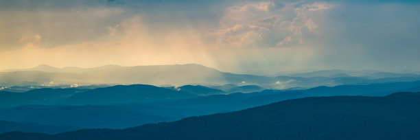 阳光透过云层照射在雾中的山脊上。山峰的全景。美丽的风景。山旅游的概念。图片下载