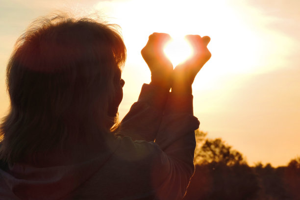 幸福的女人和双手形成一个心形与夕阳的剪影图片下载