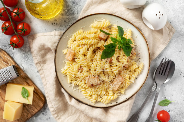 在清淡的烹饪背景下，用瓷盘盛着奶油酱火腿的意大利面。传统的意大利菜girandole在一个碗在厨房的桌子顶部的观点图片下载