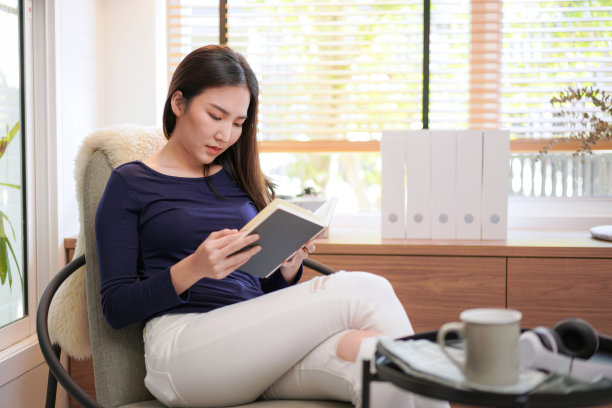 年轻的亚洲妇女坐在舒适的扶手椅上放松和阅读的书休息的假期图片下载