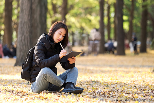 年轻女子坐在秋叶和使用平板电脑图片下载