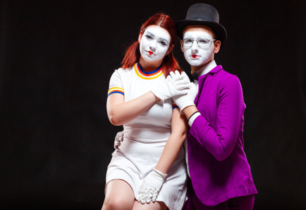 两个哑剧艺术家的肖像，孤立在黑色背景上。年轻女子坐在男子的膝盖上。象征全家福，美满夫妻图片下载