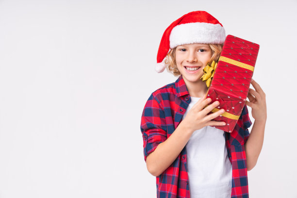 快乐的小白种人学校男孩拿着圣诞礼物礼物在圣诞老人红帽子孤立在白色的背景。2022年新年快乐!图片下载