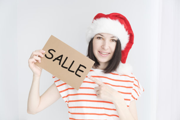 女孩戴着圣诞老人的头饰，手里拿着一张写着“salle”字样的卡片。折扣的概念。图片下载