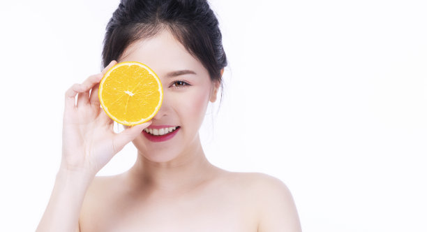 快乐的女人拿着新鲜的桔子片维生素c盖自己的眼睛好皮肤，而看着相机在孤立的白色背景。保健肤色活力或饮食生活理念。图片下载