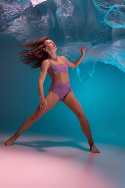 一个年轻灵活的当代舞者跳舞与织物孤立在梯度蓝白色背景在霓虹灯图片下载