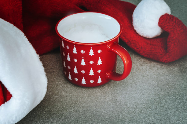 圣诞节的背景。毛茸茸的圣诞帽和红色的咖啡杯都装饰着圣诞饰品。冬天的假期。圣诞快乐，新年快乐。图片下载