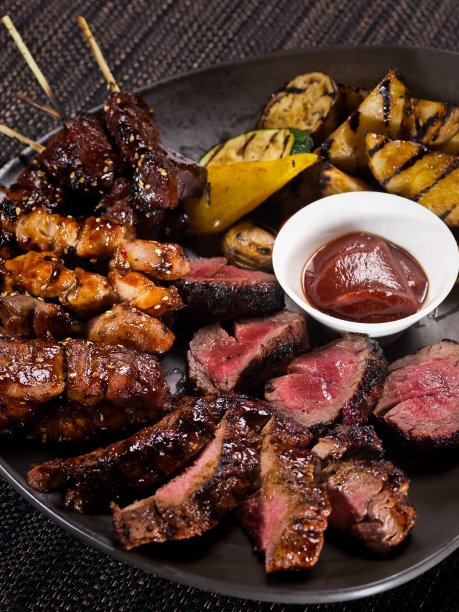 肉盘，一套不同的烤串和烤切片菲力牛排在盘子上与烤蔬菜，在黑暗的背景上的特写照片图片下载