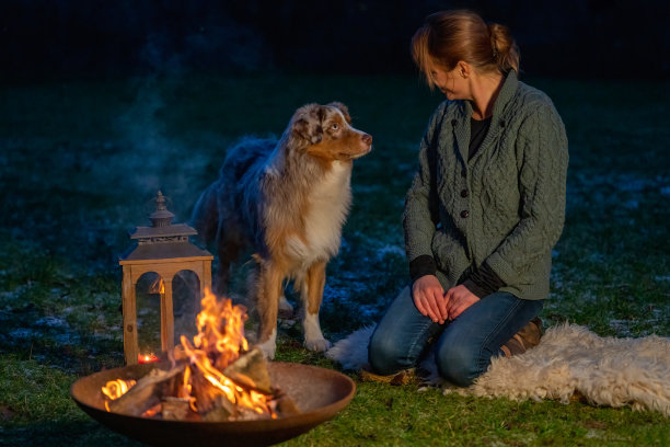 狗和他的主人坐在篝火旁。女人深情地看着德国牧羊犬。节日在冬天，蜡烛火在灯笼图片下载