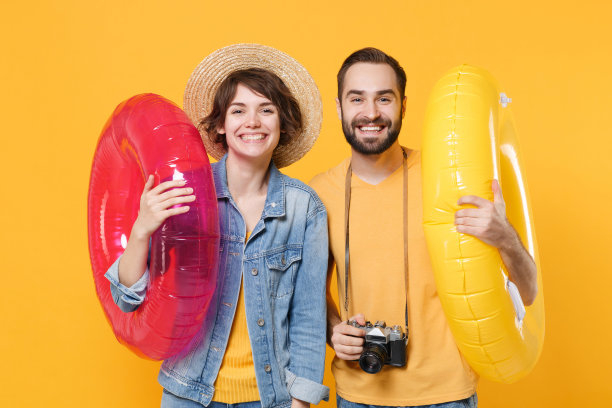 微笑的游客夫妇朋友男孩女孩在夏天的衣服帽子照片相机孤立在黄色的背景。周末出国旅游的旅客。航空飞行旅行的概念。充气环。图片下载