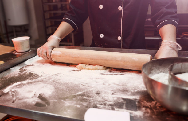 一位女面包师穿着围裙，在厨房的桌子上擀面，糕点烘焙概念蛋糕制作饼干，烘烤自制披萨在一家餐厅图片下载
