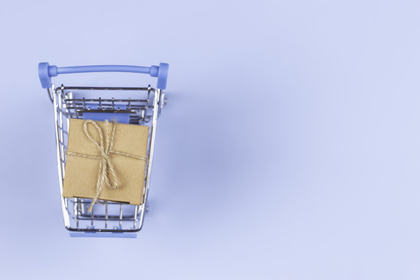 俯视图到迷你购物车与小牛皮纸礼品盒在浅蓝色的背景。电子商务，网上购物概念图片下载