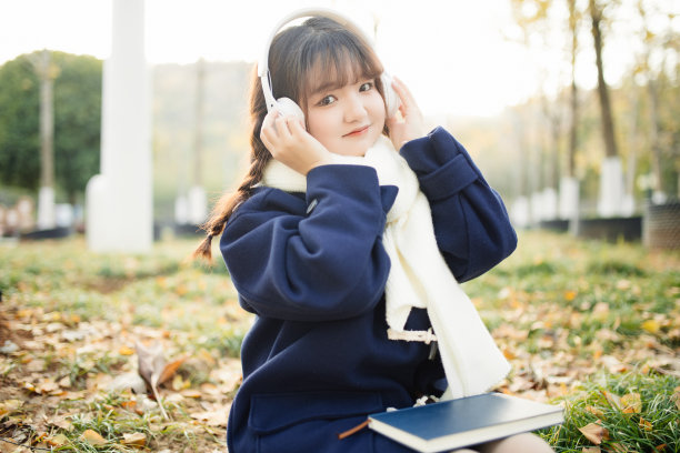 一个女大学生正在外面听音乐看书。图片下载