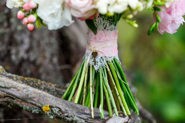 一个精致和非常美丽的婚礼花束玫瑰，牡丹，牡丹和氢化背景上的绿色植物。粉色和白色的新娘花卉。手柄装饰有蕾丝和syvmolichnym钥匙图片下载
