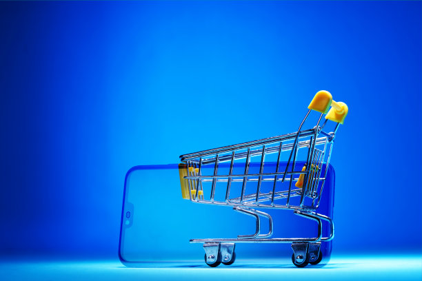 购物车与空白的智能手机屏幕上的蓝色背景。购物车。杂货店推购物车。网上购物图片下载