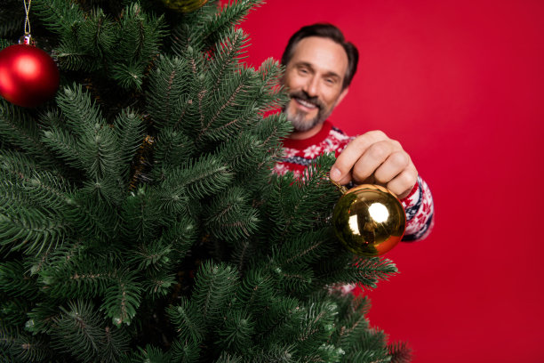 照片肖像祖父在套衫装饰与球圣诞树在冬天孤立亮红色的背景图片下载