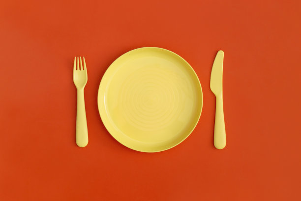 以红色为背景的带有叉子和勺子的盘子。前视图。平的。图片下载