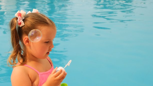 4-5岁的小女孩，穿着粉红色的泳衣，在暑假的游泳池里吹肥皂泡图片下载