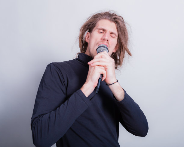 摇滚的情感肖像长发怪对着麦克风唱歌，孤立在灰色的背景复制空间图片下载