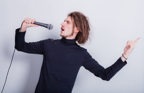 摇滚的情感肖像长发怪对着麦克风唱歌，孤立在灰色的背景复制空间图片下载