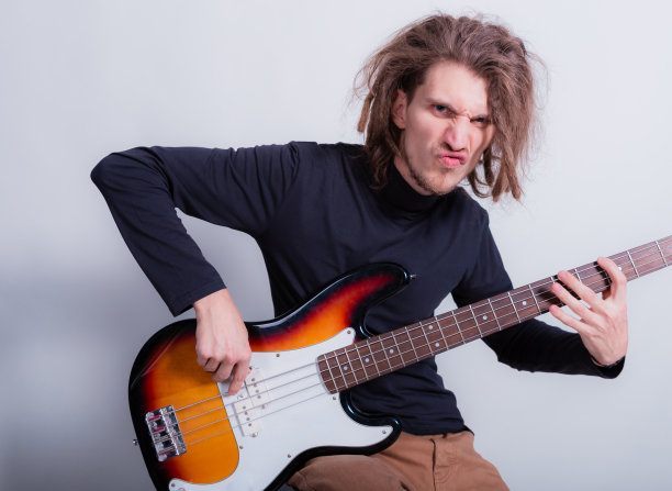 有趣的长辫男人坐在那里弹低音吉他。喜欢并热爱音乐。教育，教师，在线课程的概念在灰色的背景复制空间图片下载