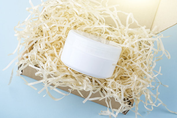 打开纸箱包装与碎纸和奶油罐在蓝色的背景。礼品工艺纸盒。生态友好的包装。天然有机自制化妆品图片下载