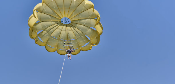 留着胡须的年长亚洲男人玩滑翔伞，看着镜头挥手致意图片下载