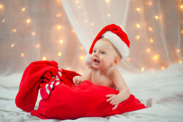 漂亮的小宝贝和圣诞老人的红袋子躺在床上。新年假期。图片下载