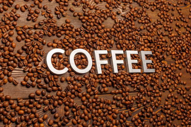 在倾斜的视角下，用烤咖啡豆覆盖的木板上镶嵌着银色字母的“咖啡”一词图片下载