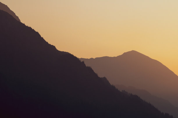 在阿拉斯加的山脉上，烟雾缭绕的橙色夕阳图片下载