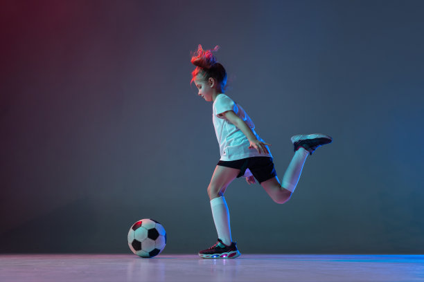 全长水平肖像的小女孩踢足球孤立的梯度蓝色背景在霓虹灯图片下载