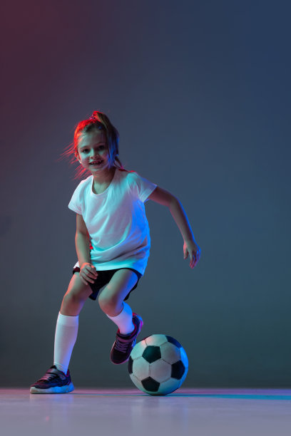 全身肖像的小活跃的女孩踢足球在霓虹灯的梯度背景孤立图片下载