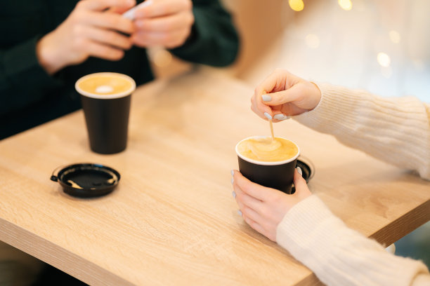 一个女人和一个男人坐在咖啡馆里，手里拿着热腾腾的咖啡杯，在桌子上聊得很开心。图片下载
