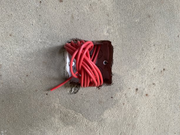从出口伸出的电线。未完成的家庭装修在白色的墙壁上。开放的电压,小心。图片下载