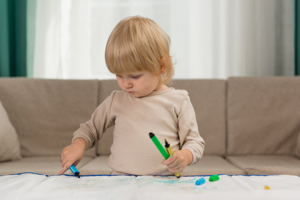 一个穿着睡衣的小女孩在家里的桌子上若有所思地用儿童水笔画画图片下载