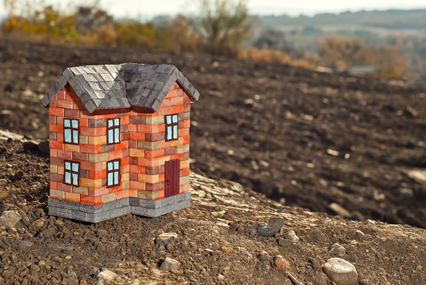 地上的砖玩具屋。棕色土地上的橙色房子。自己的住房和建筑的概念。背景是风景和树木。图片下载