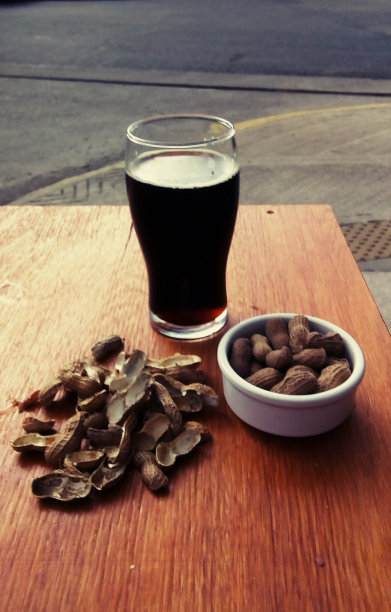 木桌上放着花生的黑色精酿啤酒图片下载
