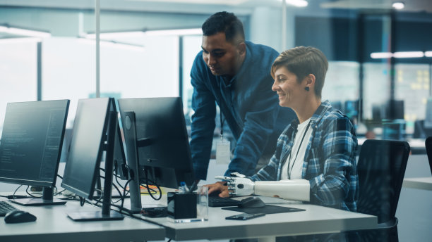 多元化包容性办公室的团队合作:项目经理与带假肢的残疾妇女在台式电脑上工作。专业软件工程师创建电子商务应用解决方案图片下载