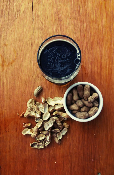 木桌上放着花生的黑色精酿啤酒图片下载