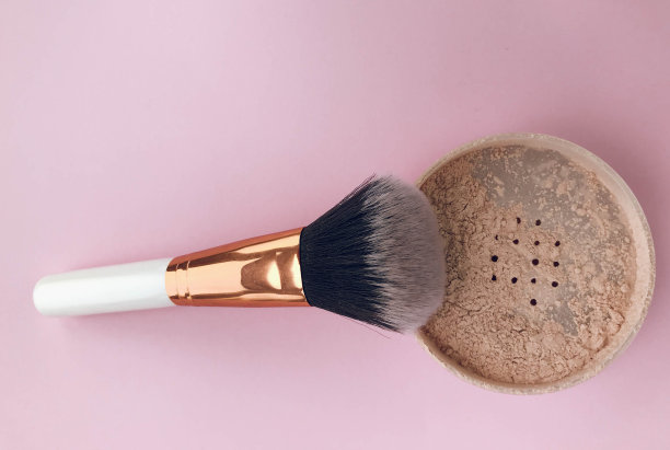 在明亮的背景上松散的粉末。白色手柄和金色绒毛托。刷子由天然材料制成。带有粉红色调的粉末图片下载